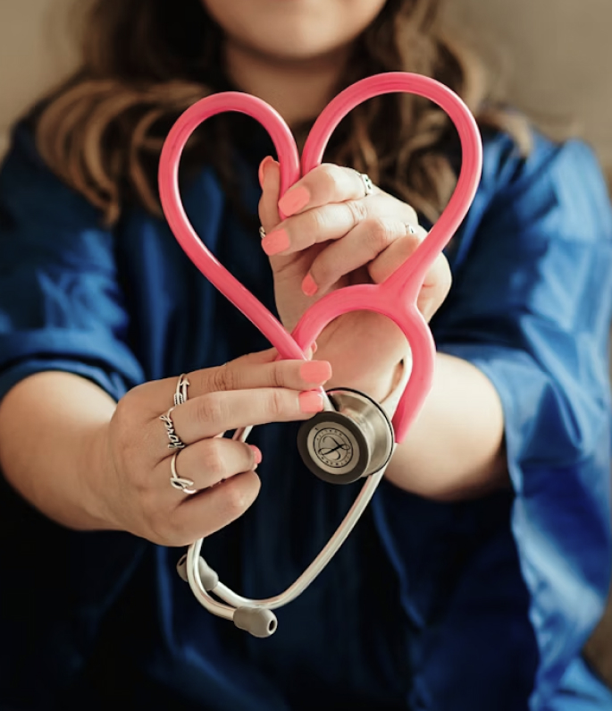 Eine Pflegefachkraft formt ein Herz aus einem Stetoskop